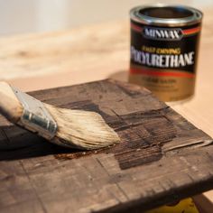 a paint brush sitting on top of a wooden board next to a can of paint