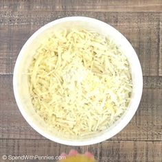 a white bowl filled with shredded cheese on top of a wooden table