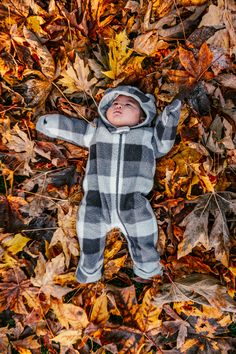 a baby is laying in leaves on the ground with his arms up and eyes closed