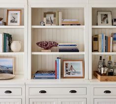 a white bookcase filled with lots of books next to drawers and pictures on top of them