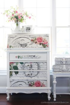 a white dresser with pink flowers on it next to a vase filled with roses and music sheets