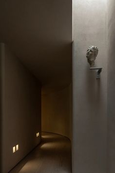 an empty hallway with light coming in from the ceiling and a plaster bust on the wall