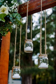 three mason jars filled with white flowers hanging from a wooden beam