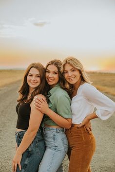 three women hugging each other in the middle of an empty road at sunset or sunrise