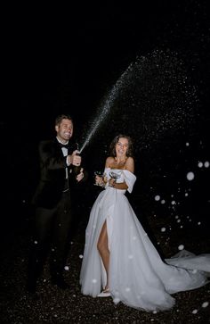 a bride and groom are standing in the rain with their arms around each other while spraying champagne into the air