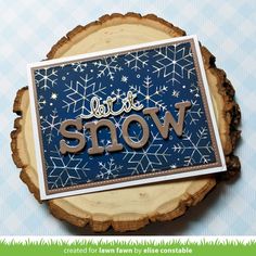 a close up of a piece of wood with the word snow on it and some snowflakes in the background