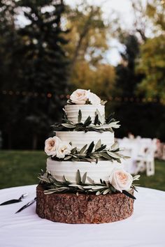 a wedding cake with white flowers and greenery on the top is sitting on a tree stump