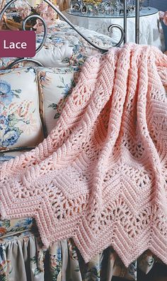 a pink crocheted blanket sitting on top of a bed next to pillows and blankets