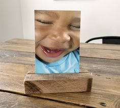 a young boy smiling with his eyes closed on a wooden table next to a piece of wood