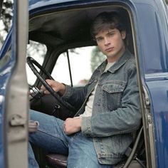 a young man sitting in the driver's seat of a blue truck with his hand on the steering wheel