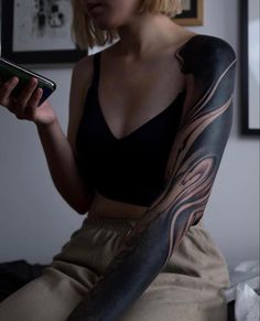 a woman with a tattoo on her arm holding a cell phone and looking at it