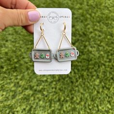 a pair of earrings that are on top of a piece of paper in front of some grass