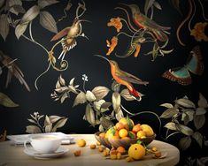 a bowl of fruit sitting on top of a wooden table next to a wall with birds and flowers