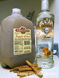 a bottle of apple cider next to some cinnamon sticks and a bottle of rum