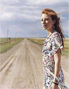 a woman standing in the middle of a dirt road with her hand on her hip