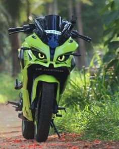 a green motorcycle parked on the side of a dirt road in front of some trees