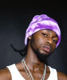 a man with a purple hat and necklaces is looking at the camera while wearing a white tank top