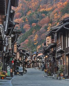 an empty street lined with wooden buildings in front of a mountain side forest filled with trees