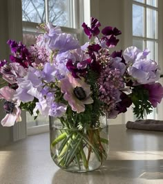 a vase filled with lots of purple flowers on top of a table next to a window