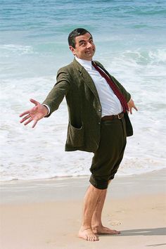 a man standing on top of a sandy beach next to the ocean wearing a suit and tie