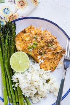 a white plate topped with rice and asparagus next to a piece of fish