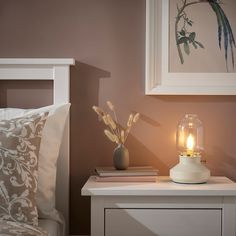 a night stand with a lamp on top of it next to a bed and pillows