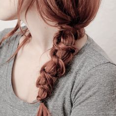 a woman with long hair in a fishtail braid wearing a gray shirt and looking off to the side