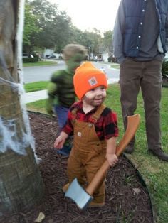 a little boy in an orange hat holding a mallet and standing next to a tree