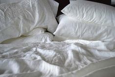 an unmade bed with white sheets and pillows