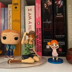 two figurines sitting on top of a book shelf