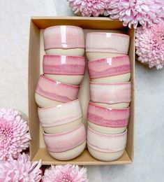 pink and white striped vases in a box with flowers around them on a table