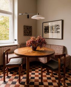 a wooden table sitting under a window next to two chairs and a vase with flowers on it