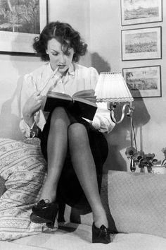 a black and white photo of a woman sitting on a bed with a book in her hand