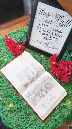 an open book sitting on top of a green doily next to a framed sign