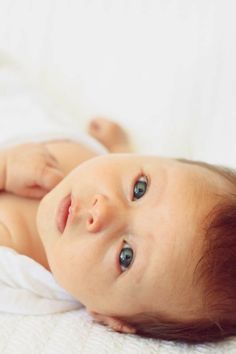 a close up of a baby laying on a bed looking at the camera with blue eyes