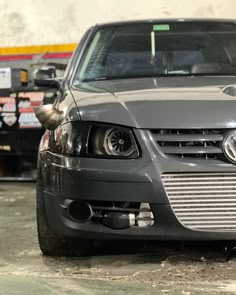 the front end of a gray car parked in a garage with other cars behind it