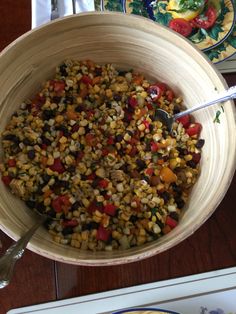 a large bowl filled with corn on top of a wooden table next to plates and utensils