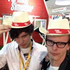 two young men wearing straw hats in front of a red and white sign that says farming simulator