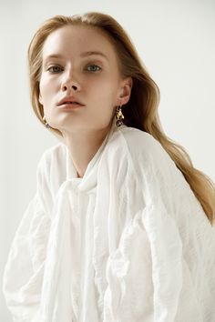 a woman with long blonde hair wearing white shirt and gold earring, looking off to the side