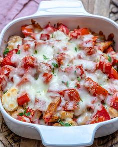 a casserole dish with tomatoes, cheese and other toppings on a wooden table