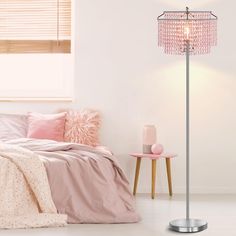 a bedroom with a bed, pink pillows and a floor lamp in front of the bed