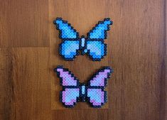 two pieces of perler bead art on a wooden surface, one with pink and blue butterflies