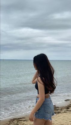 a woman standing on top of a sandy beach next to the ocean with her back to the camera