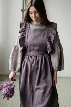 Victorian style apron with flutter sleeves is made from 100% soft and washed linen. Details: - Composition: 100% Oeko-Tex certified linen - Colour: mauve - Cross back - Length - 124 cm (49 inches) - Adjustable with buttons - Size: One size - Light weight linen - Linen care: machine wash gentle; tumble dry low, ironing optional - The price is for one pinafore dress, other pictured items are not included Measurements: Length from waist down: 80 cm (31,4 in) Chest width: 24 cm (9,4 in) without wing Pioneer Clothing, Linen Pinafore Dress, Linen Pinafore Apron, Linen Pinafore, Apron For Women, Cottagecore Clothes, Pinafore Apron, Vintage Apron, Apron Kitchen