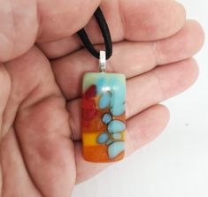 a hand holding a glass pendant with blue and orange designs on it's side