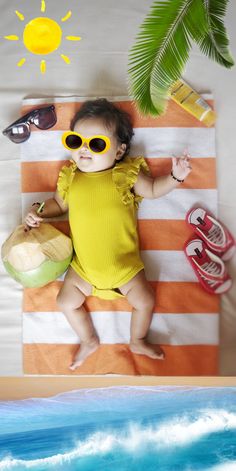 a baby wearing sunglasses laying on a towel next to the ocean with sun glasses and beach items