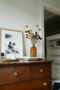 a vase with flowers on top of a wooden dresser