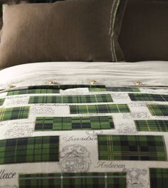 a green and white plaid comforter set on top of a bed with brown pillows