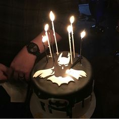 a person holding a cake with lit candles on it in the shape of a bat