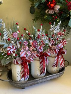 three mason jars with candy canes in them on a tray next to christmas decorations